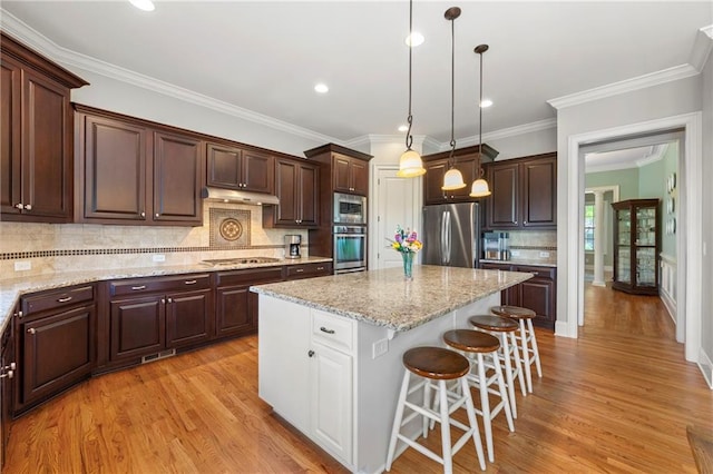 kitchen featuring dark brown cabinetry, a kitchen island, a breakfast bar, under cabinet range hood, and stainless steel appliances