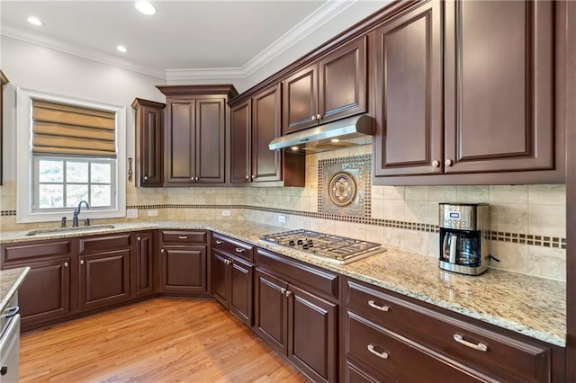 kitchen featuring crown molding, light wood-type flooring, under cabinet range hood, a sink, and stainless steel gas stovetop