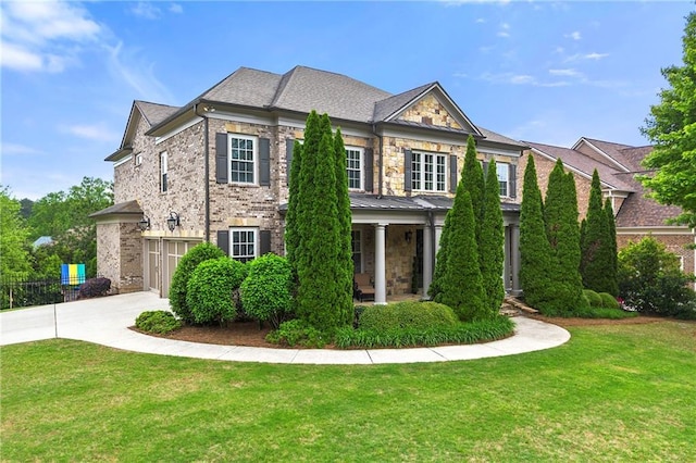 colonial inspired home featuring covered porch, a garage, a front lawn, concrete driveway, and stone siding