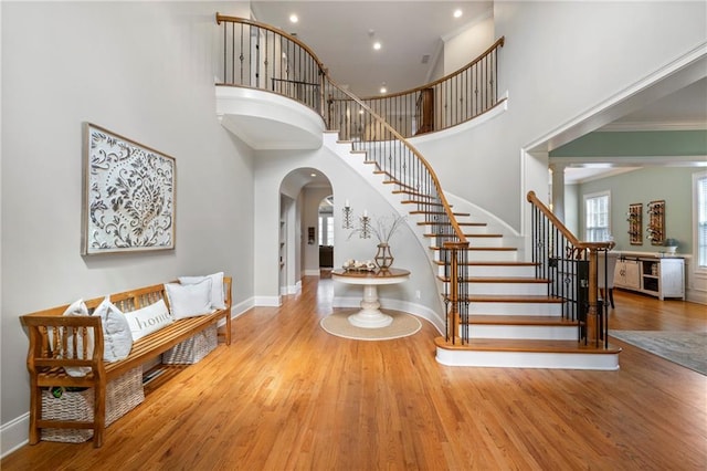 foyer entrance featuring stairway, arched walkways, a high ceiling, and wood finished floors