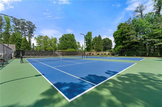 view of tennis court with community basketball court and fence