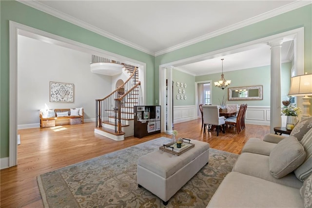 living room with crown molding, wood finished floors, stairway, a notable chandelier, and ornate columns