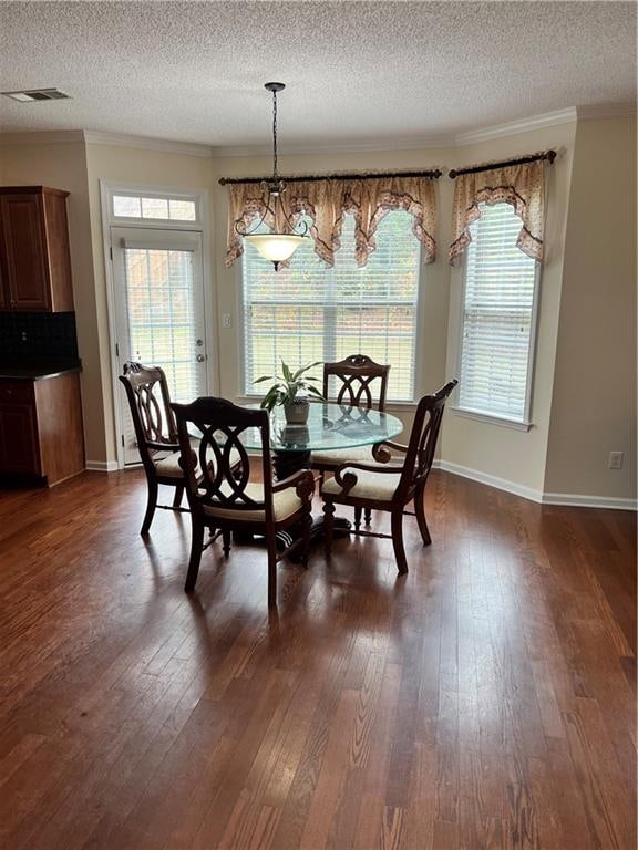 dining area with dark wood-type flooring, crown molding, a textured ceiling, and plenty of natural light