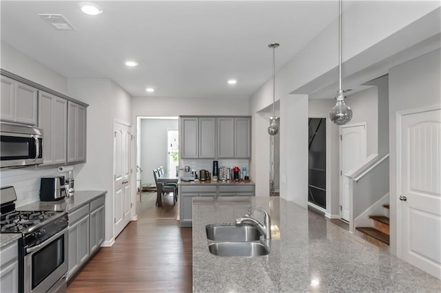 kitchen featuring decorative light fixtures, decorative backsplash, gray cabinets, appliances with stainless steel finishes, and a sink