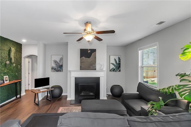 living room featuring visible vents, a fireplace with flush hearth, wood finished floors, arched walkways, and a ceiling fan