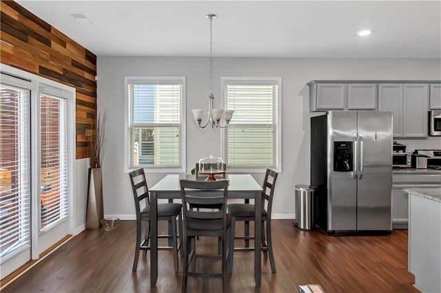 dining space featuring baseboards, an inviting chandelier, wood walls, and dark wood-style flooring