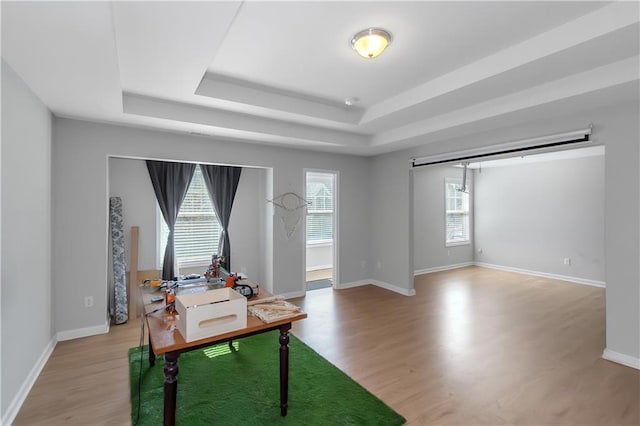 office featuring a tray ceiling, light wood-style flooring, and baseboards