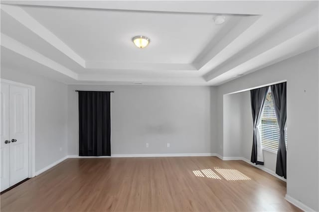 unfurnished room with a tray ceiling, baseboards, and wood finished floors