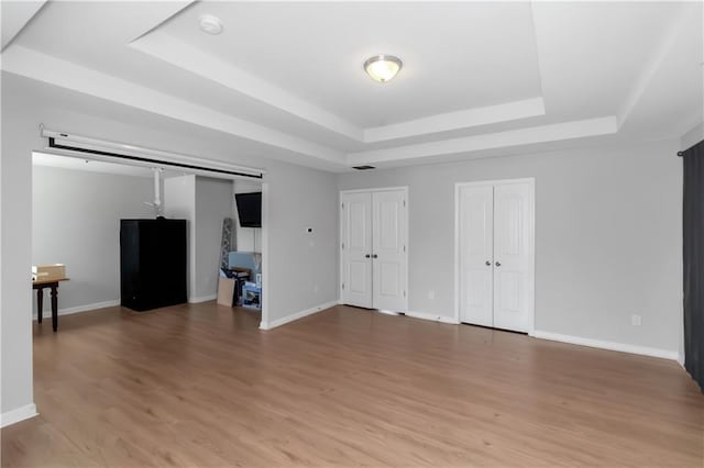 interior space with baseboards, a raised ceiling, light wood-style floors, and multiple closets