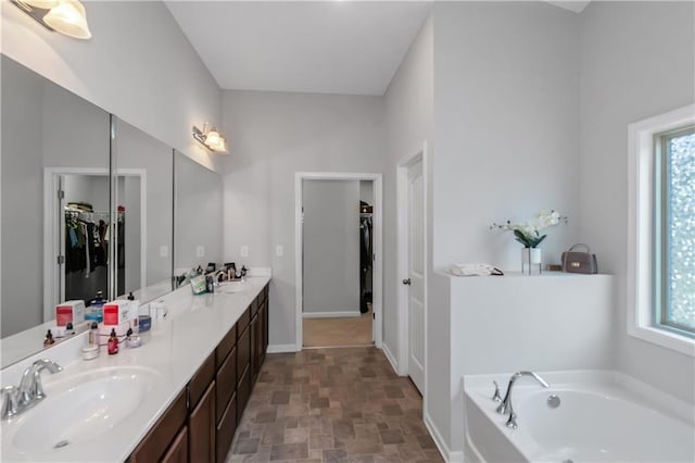 bathroom featuring a garden tub, a healthy amount of sunlight, double vanity, and a sink