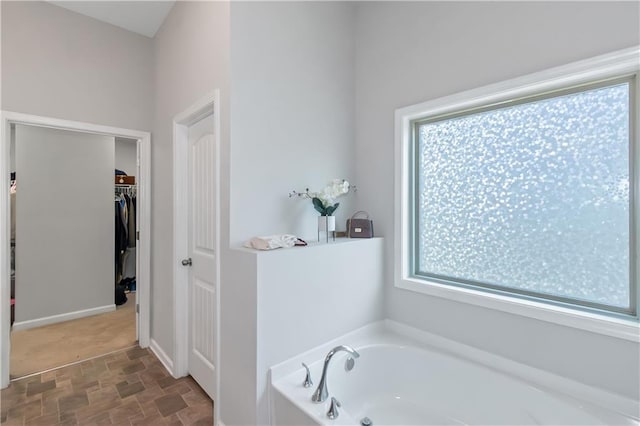 bathroom with a spacious closet, stone finish flooring, and a garden tub