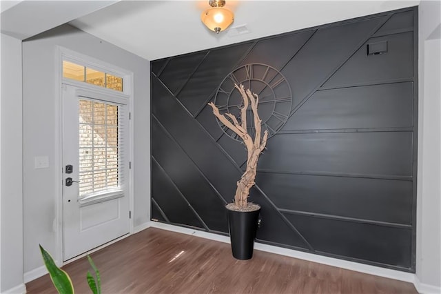 doorway featuring baseboards, wood finished floors, and an accent wall