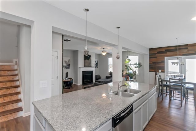 kitchen with a sink, light stone counters, stainless steel dishwasher, dark wood finished floors, and a fireplace