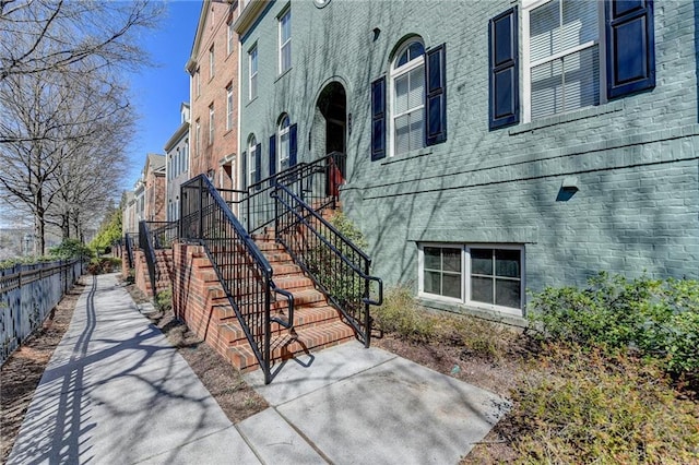 view of property exterior featuring stairs, fence, and brick siding