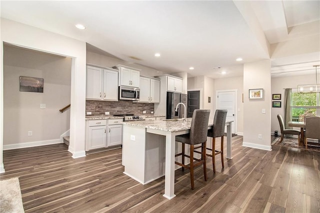 kitchen featuring appliances with stainless steel finishes, dark wood-style flooring, a kitchen island with sink, baseboards, and decorative backsplash