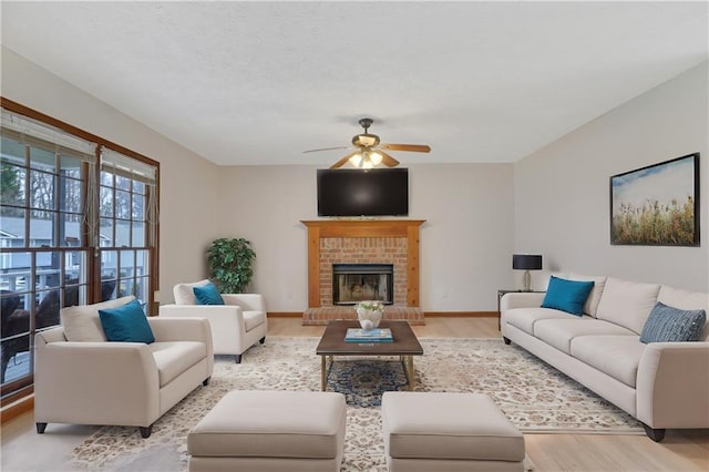 living area featuring light wood-style floors, ceiling fan, a fireplace, and baseboards