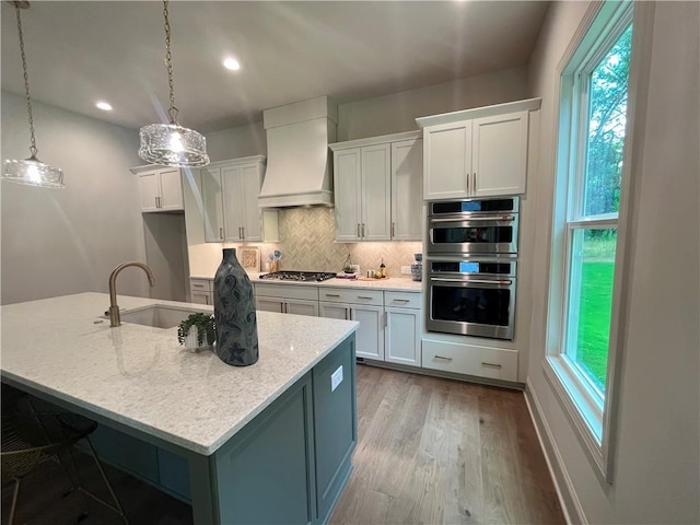 1005 Liberty Springs Dr, Woodstock, GA 30188 - kitchen featuring custom range hood, appliances with stainless steel finishes, light wood-type flooring, backsplash, and white cabinetry