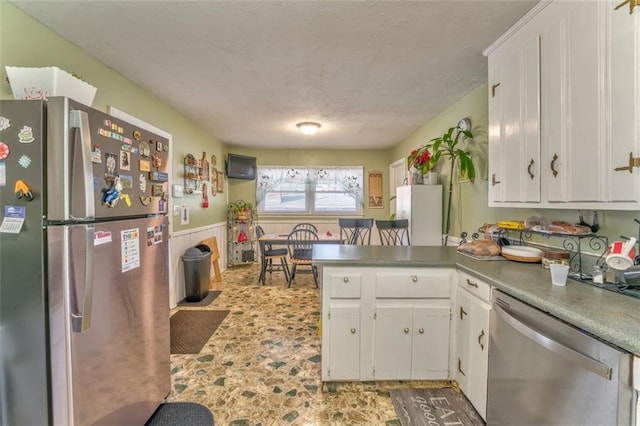 kitchen with stainless steel appliances, a wainscoted wall, white cabinets, and a peninsula