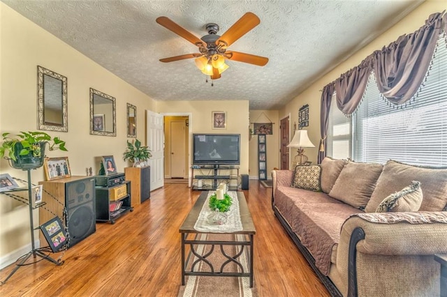 living room featuring ceiling fan, a textured ceiling, baseboards, and wood finished floors