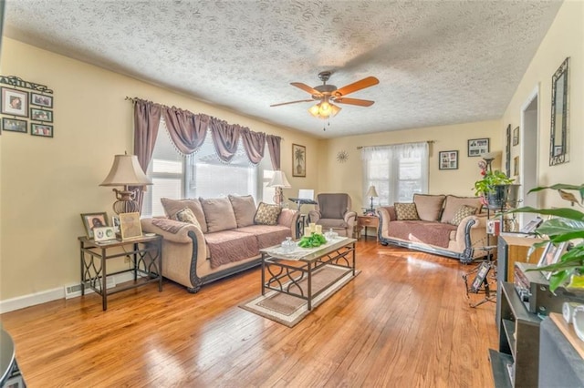 living room featuring ceiling fan, a textured ceiling, light wood-style flooring, and baseboards