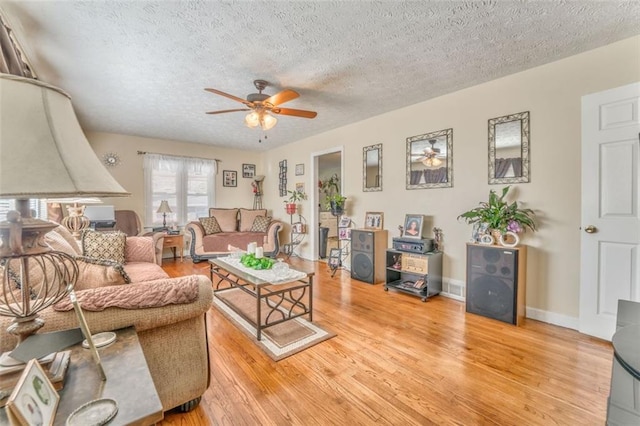 living room featuring light wood-type flooring, ceiling fan, baseboards, and a textured ceiling