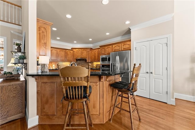 kitchen featuring a kitchen bar, ornamental molding, kitchen peninsula, stainless steel appliances, and light hardwood / wood-style floors