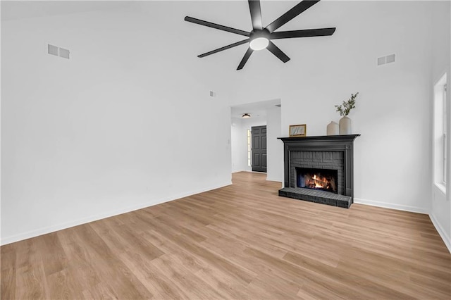 unfurnished living room with ceiling fan, a towering ceiling, a fireplace, and light hardwood / wood-style floors