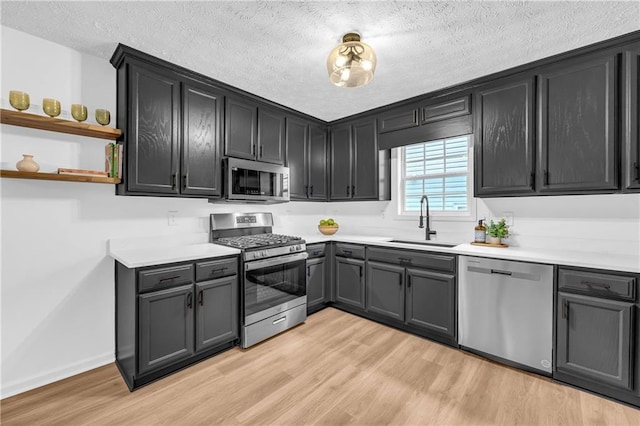 kitchen with appliances with stainless steel finishes, sink, a textured ceiling, and light hardwood / wood-style flooring