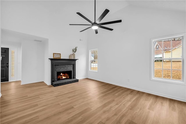 unfurnished living room with a brick fireplace, high vaulted ceiling, ceiling fan, and light wood-type flooring