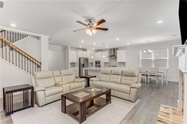 living room with a brick fireplace, crown molding, ceiling fan with notable chandelier, and light wood-type flooring