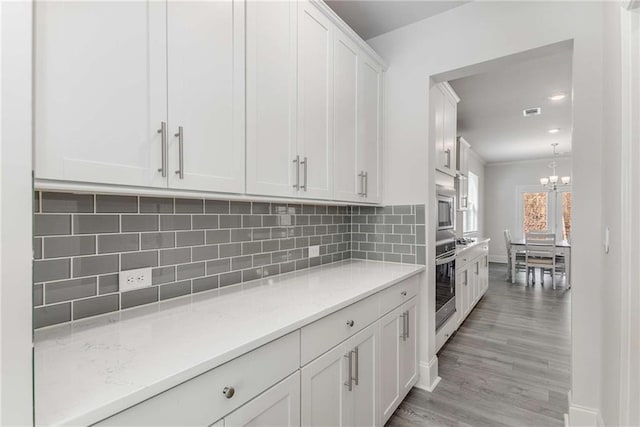 kitchen with white cabinets, decorative backsplash, appliances with stainless steel finishes, and a notable chandelier