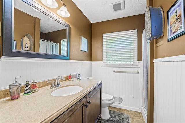 full bath with tile patterned flooring, wainscoting, toilet, and visible vents