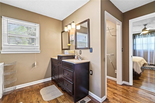 ensuite bathroom featuring baseboards, vanity, wood finished floors, and visible vents