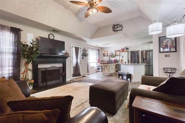 living room featuring a textured ceiling, ceiling fan, vaulted ceiling, and a fireplace