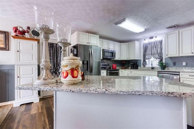 kitchen with a textured ceiling, appliances with stainless steel finishes, dark hardwood / wood-style flooring, and white cabinets