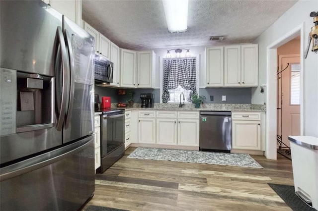 kitchen with white cabinets, appliances with stainless steel finishes, light stone countertops, dark wood-type flooring, and a textured ceiling