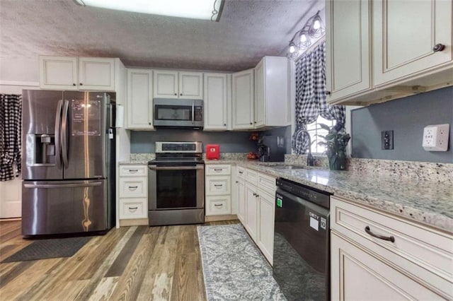 kitchen with a textured ceiling, stainless steel appliances, wood-type flooring, sink, and light stone countertops