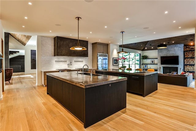 kitchen featuring pendant lighting, sink, a kitchen island with sink, and light hardwood / wood-style flooring