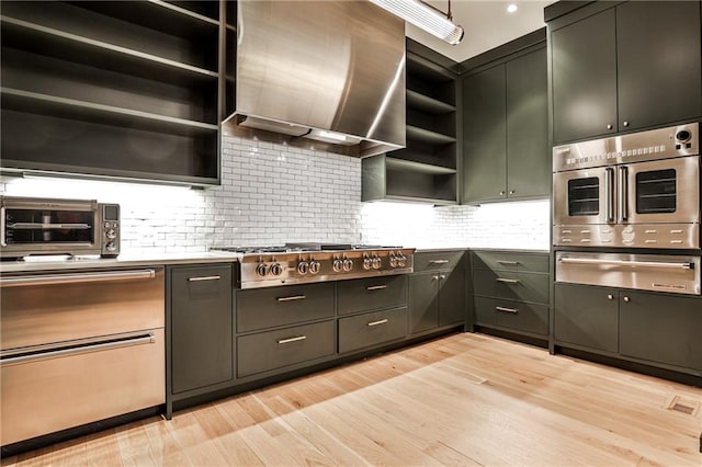 kitchen with wall chimney exhaust hood, backsplash, appliances with stainless steel finishes, and light hardwood / wood-style flooring