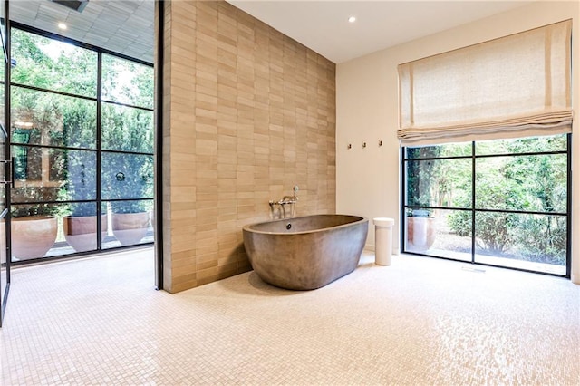 bathroom with expansive windows, a bath, and tile walls