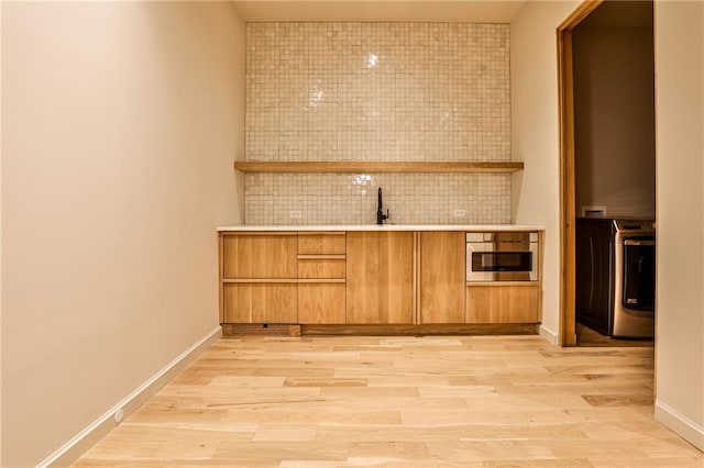 bar with decorative backsplash, light hardwood / wood-style floors, sink, washer / clothes dryer, and oven