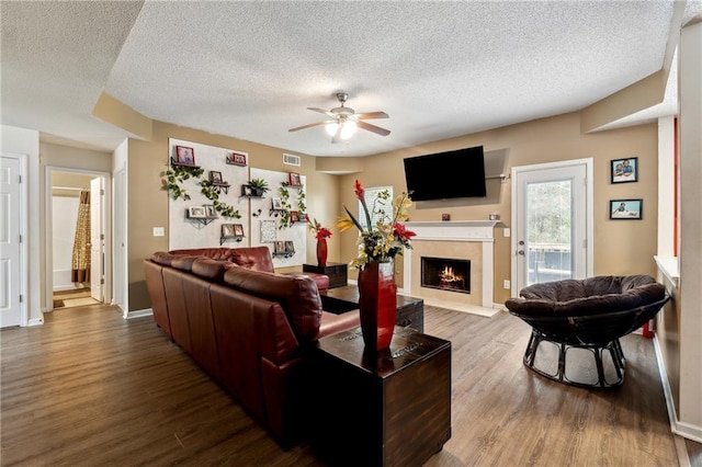 living room with visible vents, ceiling fan, wood finished floors, a lit fireplace, and a textured ceiling