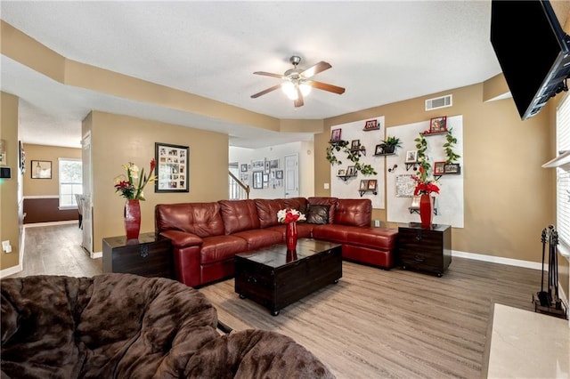 living area with a fireplace with flush hearth, visible vents, stairs, and wood finished floors