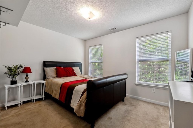 bedroom featuring light carpet, visible vents, baseboards, and a textured ceiling