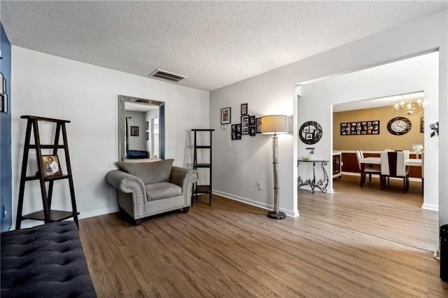 living area featuring a notable chandelier, visible vents, a textured ceiling, wood finished floors, and baseboards