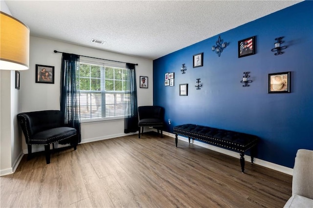 living area with a textured ceiling, wood finished floors, visible vents, and baseboards