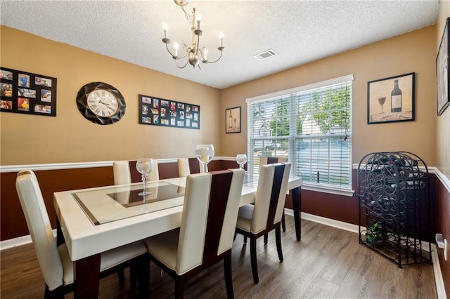 dining room with visible vents, an inviting chandelier, a textured ceiling, wood finished floors, and baseboards