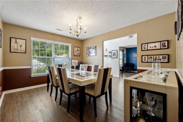 dining space featuring a textured ceiling, visible vents, a chandelier, and wood finished floors