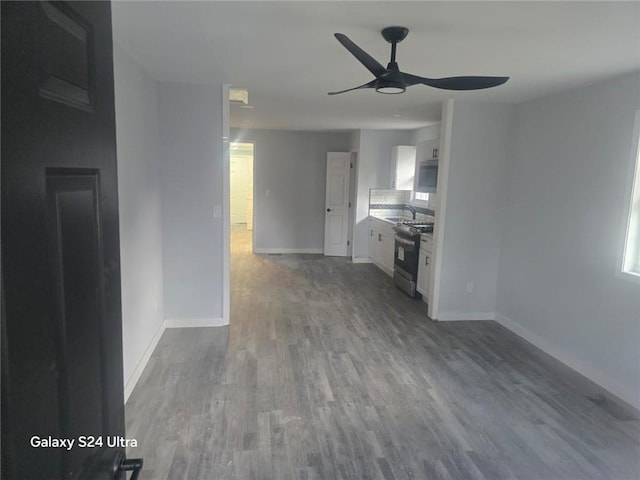 unfurnished living room featuring a ceiling fan, baseboards, and wood finished floors