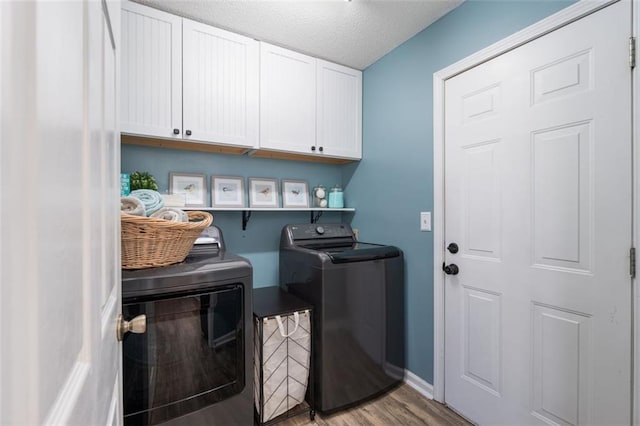 clothes washing area with washer and dryer, cabinets, a textured ceiling, and light wood-type flooring